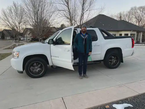 Alex standing in front of his new white Chevrolet Avalanche.